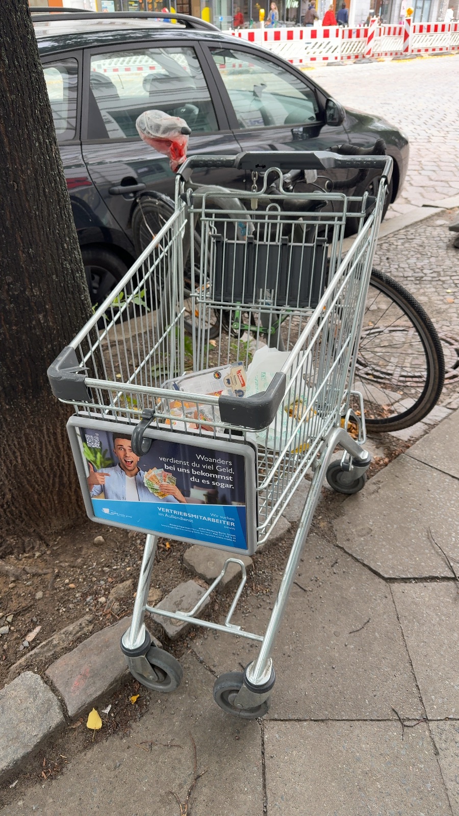 Ein Einkaufswagen eines Discounters steht auf dem Gehweg neben einem Baum, mit verschiedenen Gegenständen gefüllt, Marienburger Straße 14B, Pankow